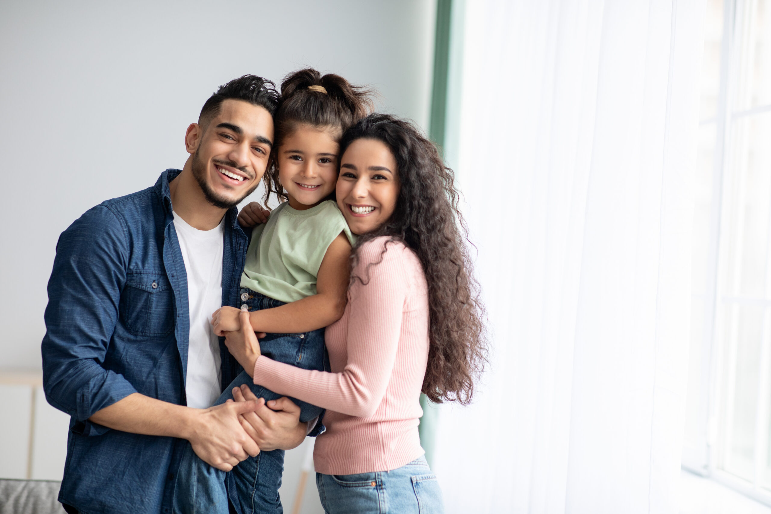 Smiling parents holding their young daughter at home, a happy family patient of Innovative Dental & Orthodontics, family dentist in Oviedo, FL